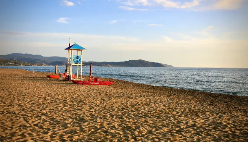 Torre di salvataggio e barche rosse sulla sabbia dorata, con il mare calmo e le colline sullo sfondo. Paestum mare.