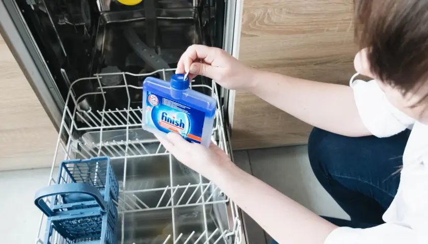 Osoba trzymająca w otwartej zmywarce niebieską butelkę z czyścikiem Finish.