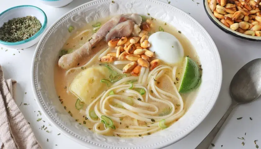Un reconfortante caldo de gallina peruano con fideos, huevo duro, papa, choclo y un toque de limón.