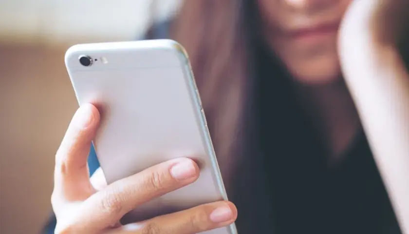 Kobieta trzyma telefon, zastanawiając się, jak wysłać mms.