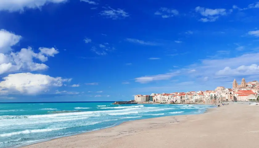 Spiaggia di Palermo con mare turchese e case bianche con tetti rossi.