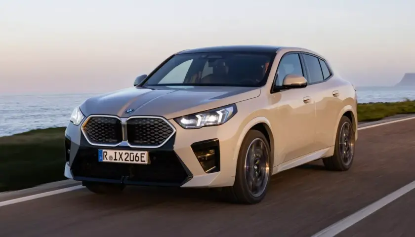 Nowy, beżowy BMW iX2 jedzie wzdłuż wybrzeża.