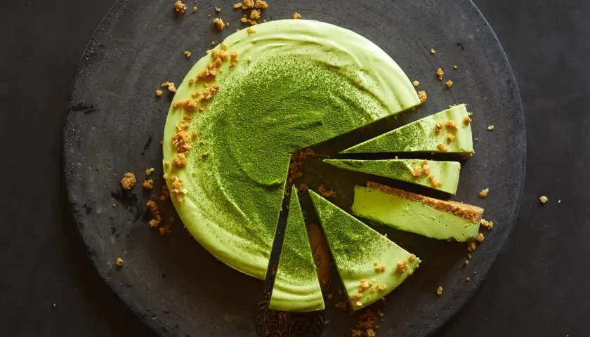 Ein köstliches Matcha-Dessert, in Stücke geschnitten, mit zerbröselten Keksen und feinem Matcha-Pulver bestreut.