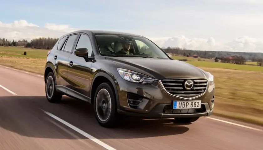 Brun Mazda CX-5 kör på en landsväg i Sverige. Föraren verkar ha ett problem med bilen.