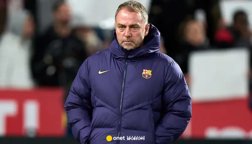 Zamyślony trener Barcelony w granatowej kurtce z herbem klubu.