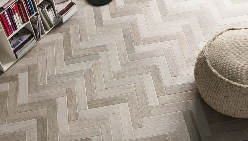 Un elegante pavimento ruvido interno in parquet a spina di pesce, con una libreria e un pouf.