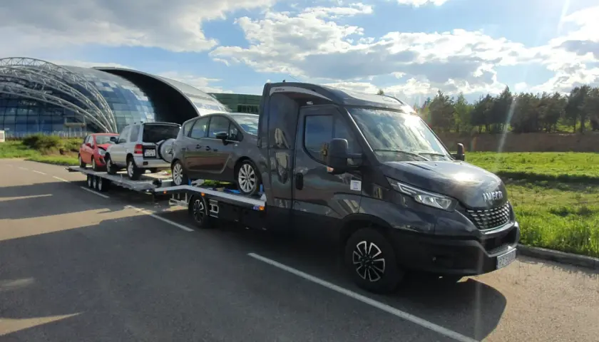 Laweta z autami pod nowoczesnym budynkiem, jak dojadę rzeszów? Słońce i chmury na niebie.