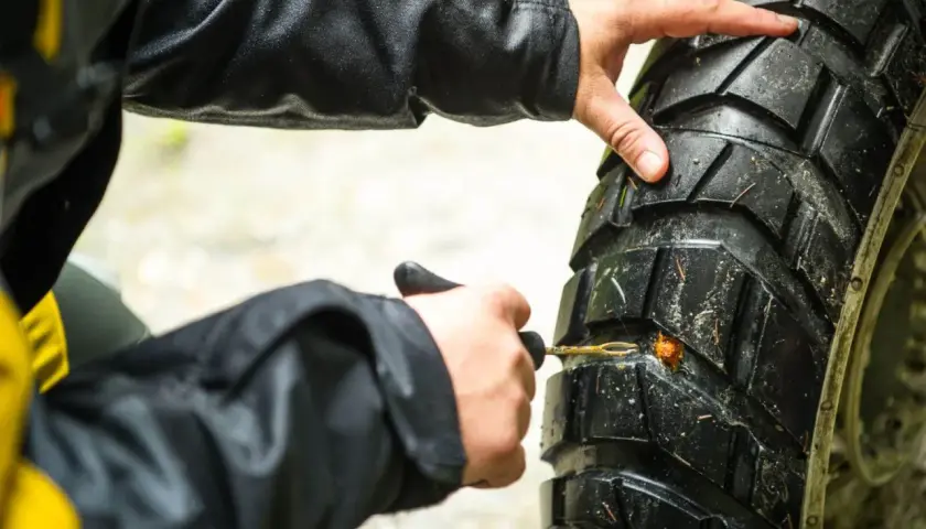 Manos arreglando pinchazo moto con kit de reparación.