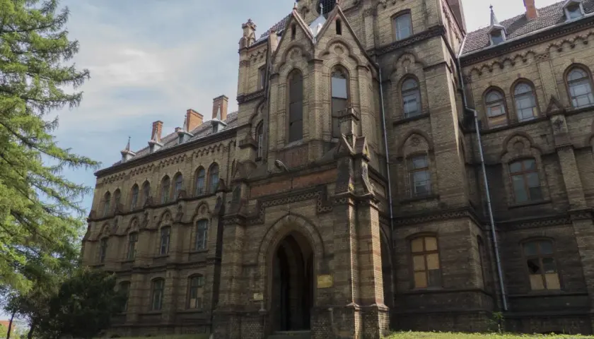 Mokrzeszów pałac, monumentalna budowla z cegły, z charakterystycznymi łukami i wieżyczkami, otoczona zielenią.