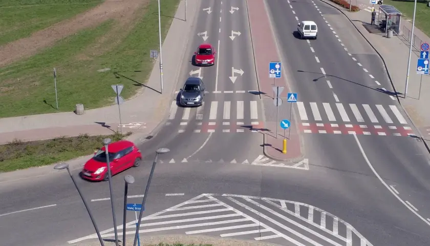 Samochody poruszają się po skrzyżowaniu z oznakowaniem sugerującym rondo turbinowe.