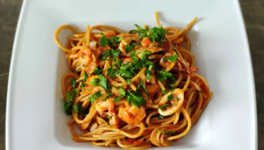 Pyszne spaghetti z owocami morza, krewetkami i kalmarami, posypane świeżą natką pietruszki.