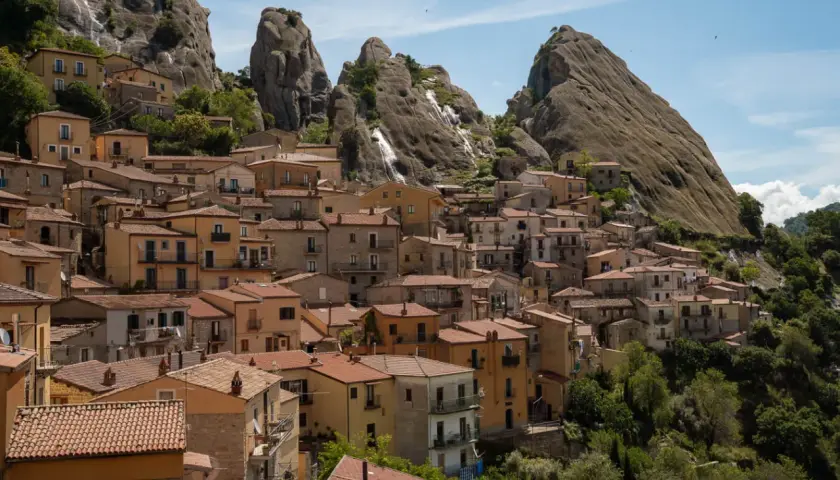 Houses cling to a mountainside in Pietrapertosa, Italy, beneath dramatic rock formations.