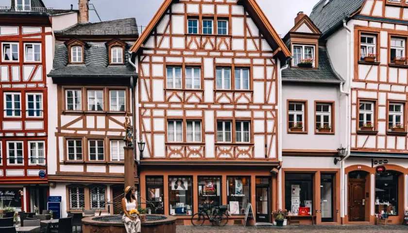 Fachwerkhaus-Idylle in Mainz. Eine Frau sitzt am Brunnen, umgeben von malerischen Gassen – hier sind die echten Mainz Geheimtipps!