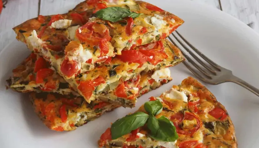 Une part d'omelette aux légumes colorée, garnie de tomates, courgettes et fromage frais, avec une feuille de basilic.