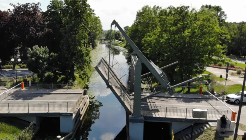 Podniesiony most zwodzony w Nowym Dworze Gdańskim, nad kanałem otoczonym zielenią.