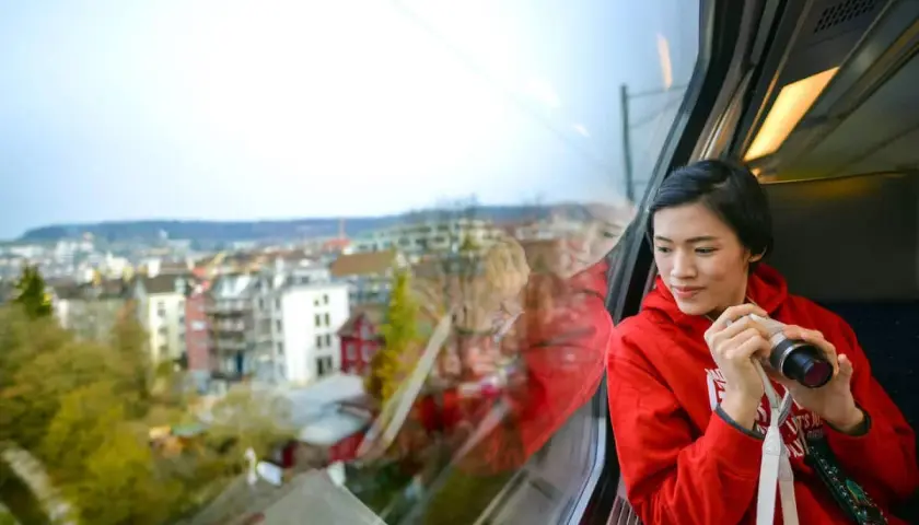 Joven en tren, con cámara, mirando el paisaje urbano. Quizás viajando en un tren de Tarragona a Sevilla.