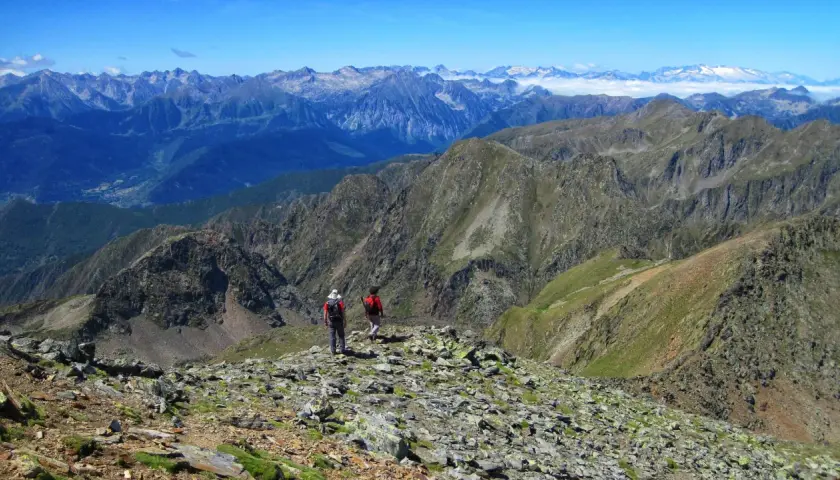 Dos excursionistas exploran las impresionantes **rutas de Esterri d'Àneu**, rodeados de picos montañosos y un cielo azul.
