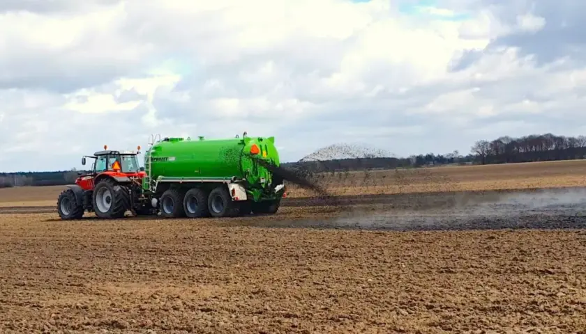 Czerwony traktor z zielonym wozem asenizacyjnym rozprowadza poferment z biogazowni na polu.