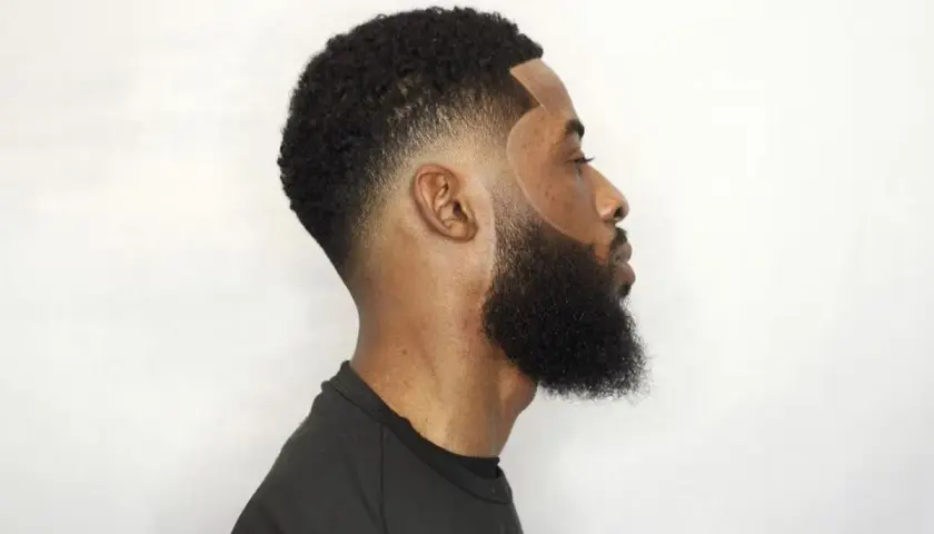 Hombre con barba tupida y corte de pelo con taper fade bajo, líneas definidas y degradado impecable.