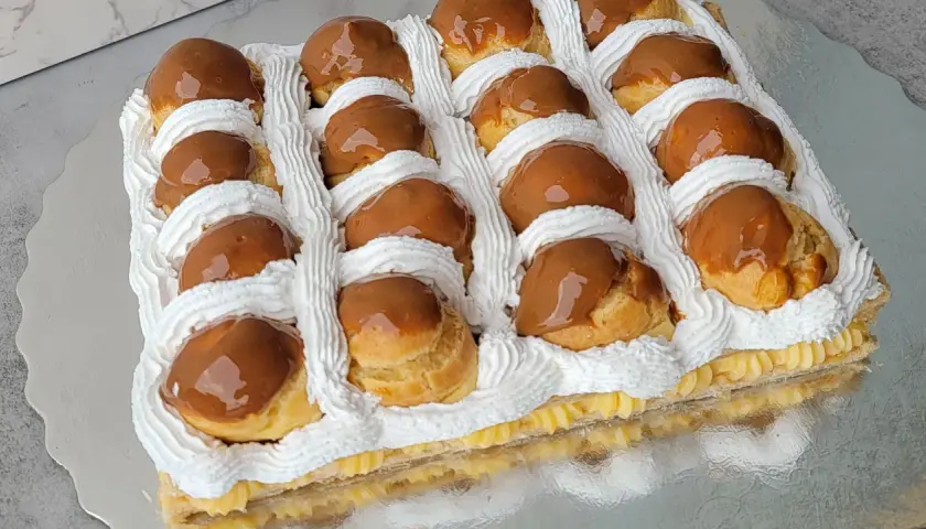 Deliciosa torta rellena de crema pastelera y cubierta con profiteroles bañados en dulce de leche y decorada con crema chantilly.