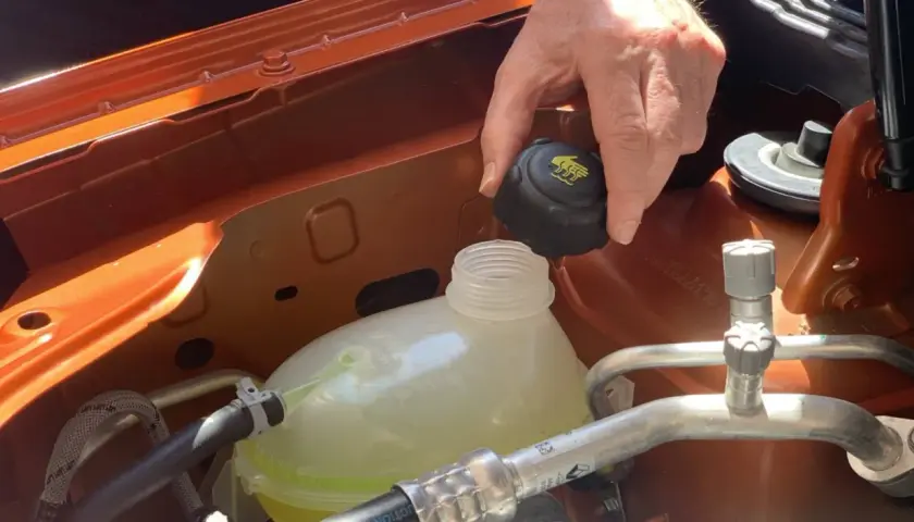 Mano quitando el tapón del depósito de anticongelante, que parece bajo. El anticongelante se evapora con el tiempo.