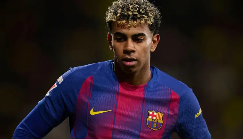 Młody piłkarz Lamine Yamal w koszulce FC Barcelony, z charakterystyczną fryzurą i skupionym spojrzeniem.