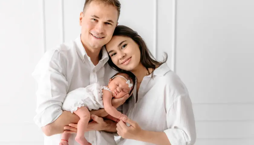 Szczęśliwa rodzina z noworodkiem w białych ubraniach, pozująca do sesji zdjęciowej.