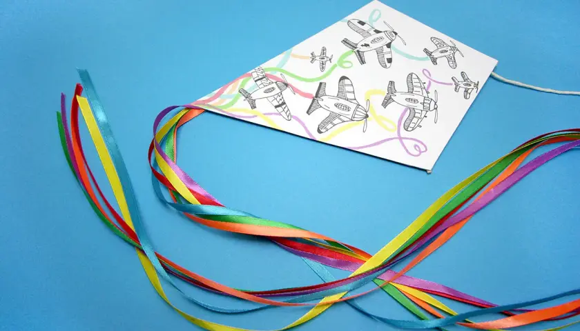 Kolorowy latawiec DIY z rysunkami samolotów i tęczowymi wstążkami.