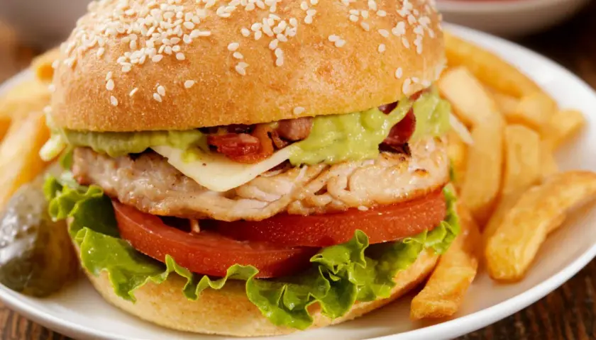 Pyszny burger z kurczakiem, z awokado, serem i chrupiącym bekonem, podany z frytkami.