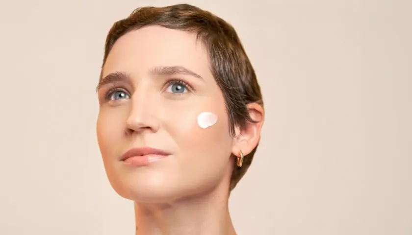 Visage d'une femme avec une touche de crème sur la joue, évoquant la protection contre le soleil pendant une hormonothérapie.