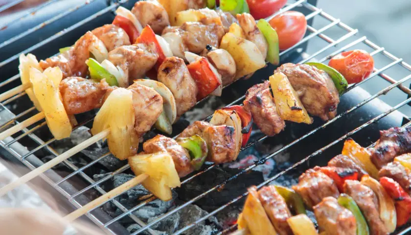 Na grillu piecze się kilka szaszłyków z kurczakiem, ananasem, papryką i pomidorkami.