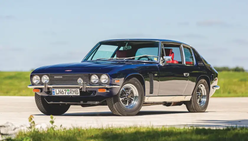 Mörkblå Jensen Interceptor med röda säten, parkerad utomhus på en solig dag.