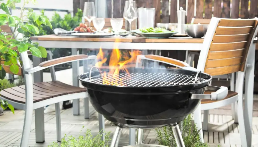 La grille bbq est prête pour un festin en plein air. Des flammes dansent sur les braises, promettant des saveurs estivales. La table est dressée, invitant au partage.