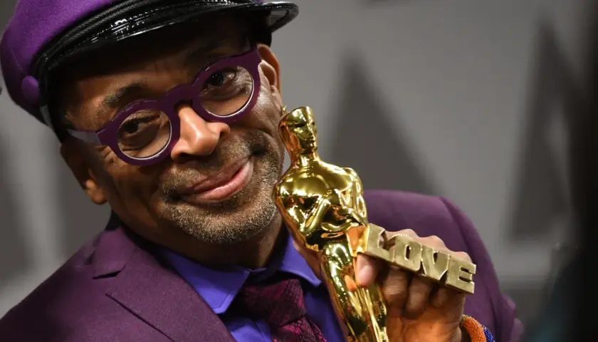 Spike Lee, w fioletowym garniturze i czapce, trzyma Oscara z napisem "LOVE". Jego filmy często poruszają ważne tematy społeczne.