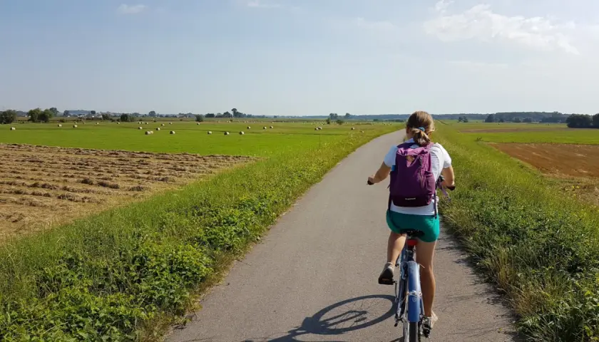 Dziewczynka na rowerze przemierza malowniczą wiślaną trasę rowerową Niepołomice, mijając pola z sianem i zielone łąki.