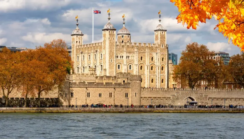 Jesienna panorama Londynu z twierdzą Tower i rzeką Tamizą. Liście drzew mienią się złotem.