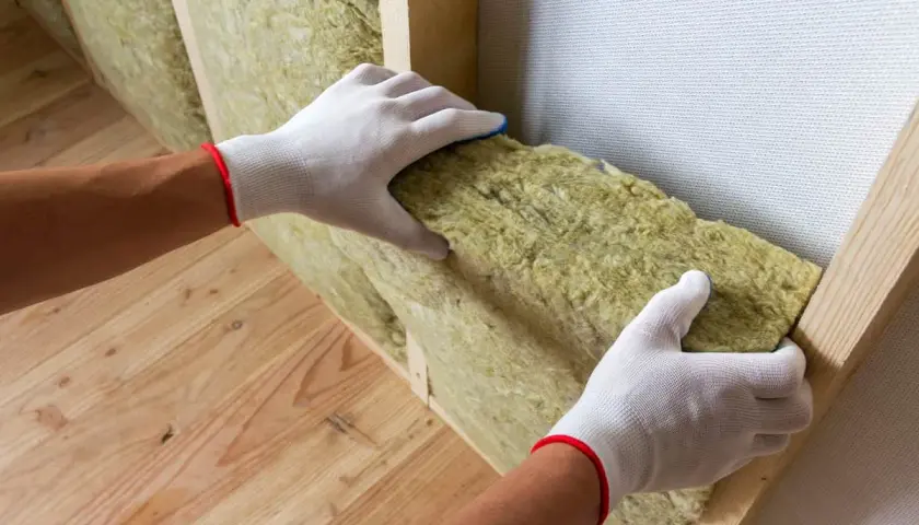 Mains gantées installant un isolant minéral dans une structure en bois pour une isolation intérieure efficace.
