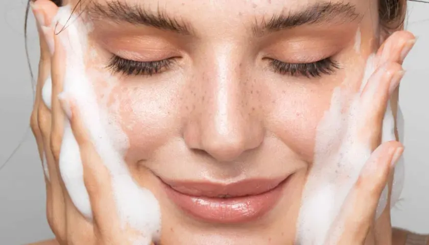 Une femme se nettoie le visage avec de la mousse. Un geste simple pour un teint frais, découvrez comment nettoyer son visage pour une peau éclatante.