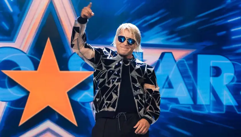 Skolim w błyszczącej kurtce i okularach przeciwsłonecznych pozdrawia publiczność na tle sceny z napisem "STAR".
