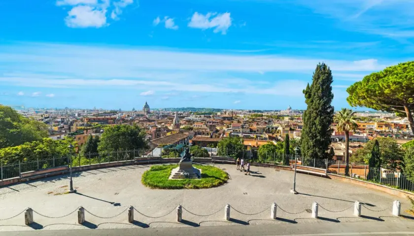 Vista panoramica di Roma con cupole e tetti, un monumento al centro e persone che passeggiano. Un'emozione da vivere a Roma gratis.