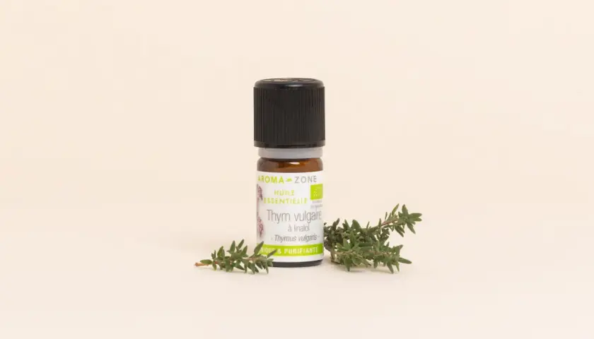 Flacon d'huile essentielle de thym vulgaire, aux notes aromatiques et purifiantes, posé à côté de brins de thym frais.