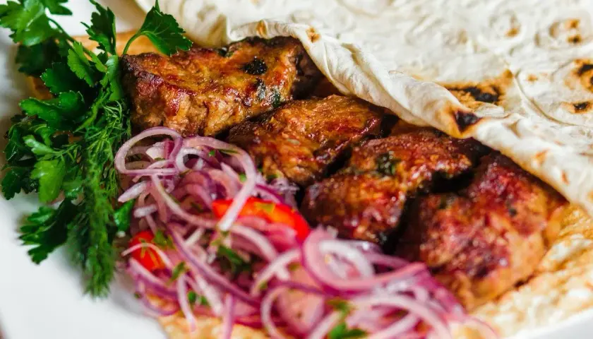 Soczyste mięso kebab zawinięte w placek, podane z czerwoną cebulą i świeżą natką pietruszki.