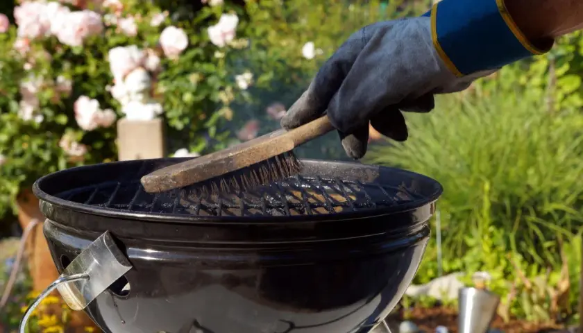 Mit einem Handschuh wird der Grillrost gereinigt. Rauch steigt auf, während die Bürste über die Roste fährt.