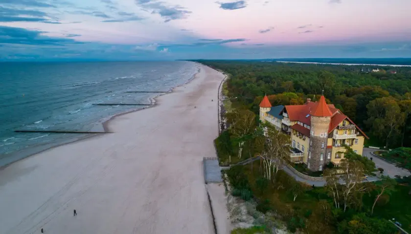 Zachód słońca nad morzem w Łebie. Piękna plaża, las i zabytkowy budynek przypominający zamek.
