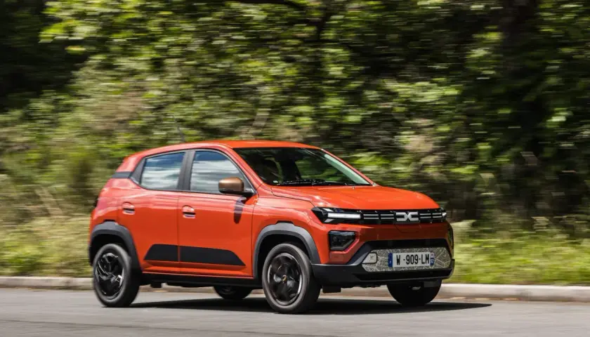Auto arancione in movimento, con cambio automatico, su strada circondata da alberi sfocati.
