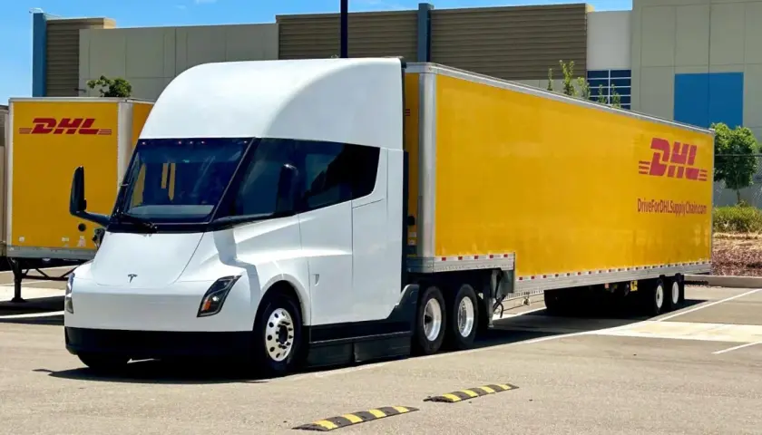 Biały Tesla Semi z żółtą naczepą DHL stoi na parkingu.