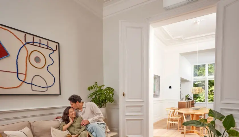 Pareja feliz en un salón moderno. El aire acondicionado Daikin, símbolo de calor confortable, se ve en la pared.
