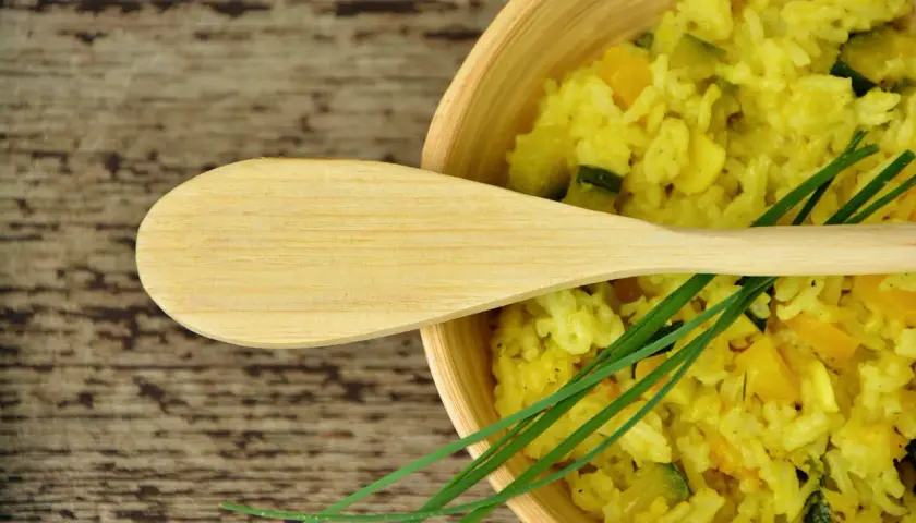 Risotto allo zafferano cremoso con zucchine e peperoni, guarnito con erba cipollina e un cucchiaio di legno.