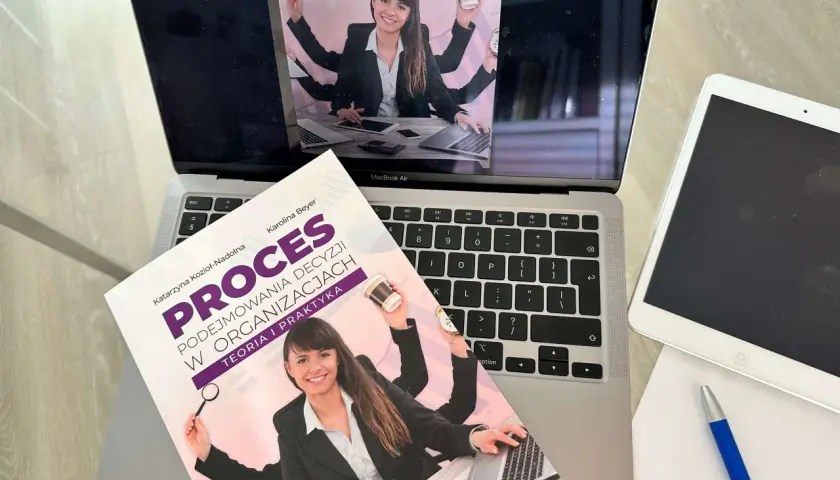 Książka "Proces podejmowania decyzji w organizacjach" na laptopie. Ilustracja sugeruje teorię racjonalnego wyboru, gdzie wieloręka kobieta zarządza wieloma zadaniami.