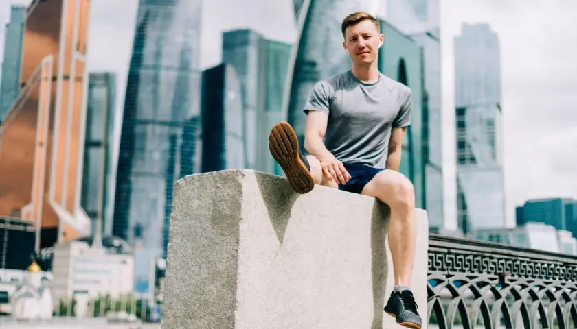 Mężczyzna w sportowym stroju siedzi na kamiennym postumencie, w tle nowoczesne wieżowce. Czasem czuję, że nie mogę złapać oddechu podczas biegania.
